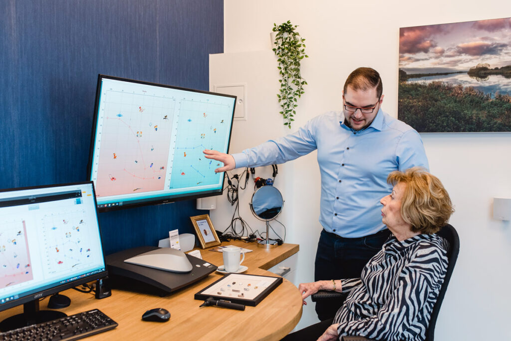 Mitarbeiter erläutert Hörprofil auf Bildschirm, Kundin blickt aufmerksam hin.