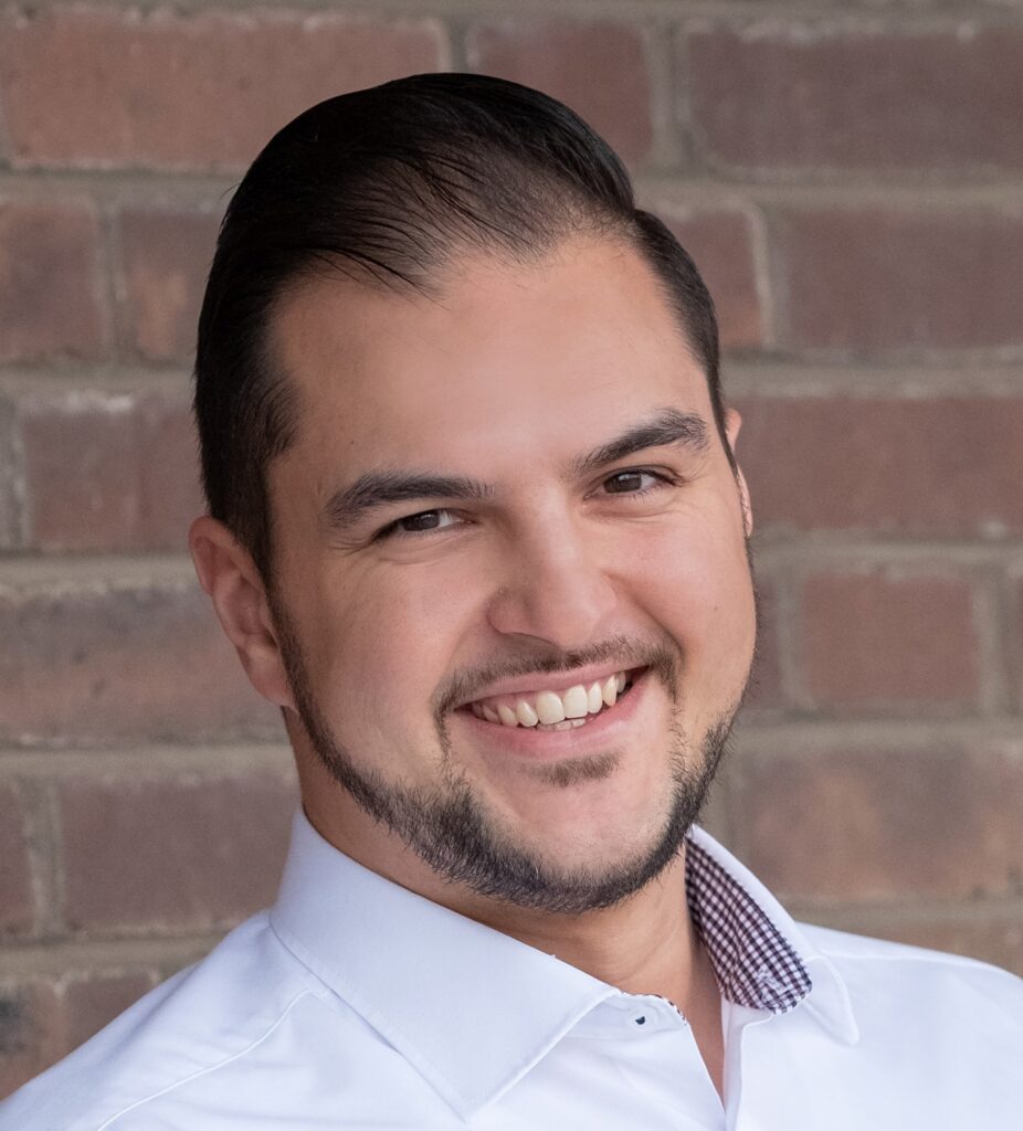 Ein junger Mann mit dunklen Haaren lächelt freundlich in die Kamera.